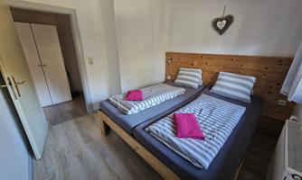 A cozy bedroom with two beds and striped bed sheets. There is a wardrobe and a warm, inviting ambiance.