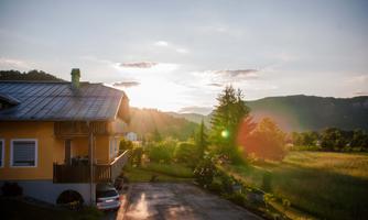 A house in a rural setting with a beautiful view of the mountains. The sun rises and illuminates the landscape.