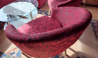 A cozy living area with two red armchairs and a glass table. The floor is covered with a decorative rug.