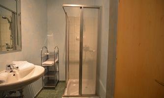 A modern bathroom with a shower and a sink. The walls are painted in a gentle blue, and there are towels on a shelf.
