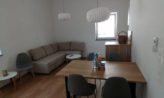 A modern living room with a bright couch and a dining table. The walls are in neutral colors and there are large windows that let in plenty of light.