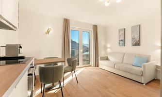 A modern apartment with a cozy seating area and a table. Large windows provide a view of the mountains.