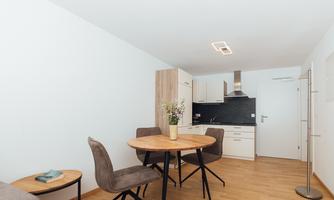 A modern kitchen with a round table and elegant chairs. The room is bright and well-furnished.