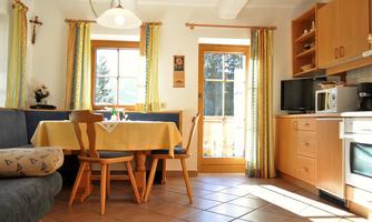 A bright and cozy kitchen with a table and chairs. Plenty of daylight comes through the window, and there are wooden furniture and colorful curtains.