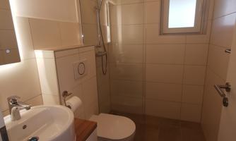 A modern bathroom with a shower, sink, and toilet. The walls are brightly tiled and there is a small window for natural light.