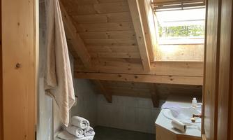 A bright bathroom with wooden walls and a skylight. There is a toilet area and a washbasin with towels.