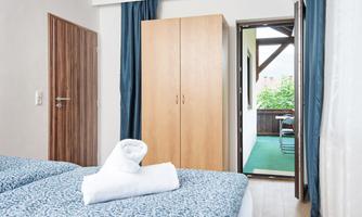 A bright room with two beds and fresh towels. In the background, there is a door to a balcony with a view of the outdoors.