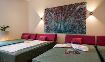 A cozy room with three beds and a colorful wall decoration. The seating area is modern and invitingly designed.