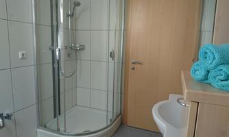 A modern bathroom with a shower and white tiles. Clean turquoise towels are on the shelf.