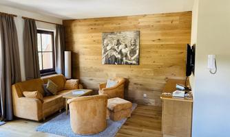 A cozy living room with wooden walls and a comfortable seating area. A TV and a piece of artwork on the wall give the room character.