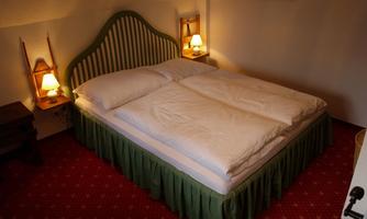 A cozy bedroom with a double bed and soft lighting. The floor is covered with a red carpet, and the walls are simply decorated.