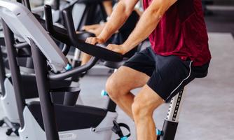 A man with a beard is working out on a stationary bike in a modern gym. In the background, another person is engaged in training.