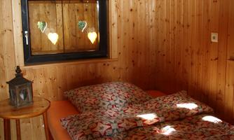 A cozy bedroom with wooden walls and a large bed.  
On the bedside table, there is a lantern, and the window has hearts as decoration.