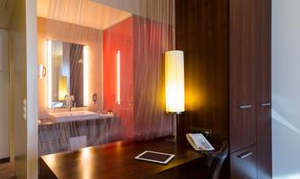A modern room with a desk and a stylish lamp. In the background, there is a bathroom area with a mirror and sink.