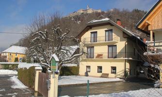 A charming house in the snow with a clear blue sky. In the background, a hill with a castle is visible.