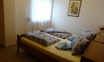 A simple bedroom with a double bed and colorful bedspreads. A window provides natural light and a cozy atmosphere.