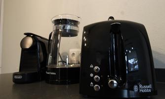 A black kitchen appliance series from Russell Hobbs, including a coffee machine, a kettle, and an espresso machine. The devices are designed to be modern and elegant.