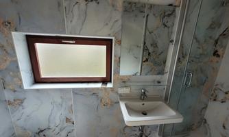 A modern bathroom with marble walls and a small window. There is a sink and a shower.