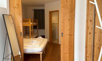 A bright room with two beds and wooden ceilings. In the foreground stands a large mirror and the walls are also designed in a wood look.