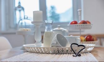 A laid table with a white serving platter, on which there are a carafe, cups, and apples. The light falls through a window and creates an inviting atmosphere.