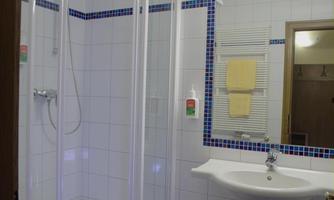 A modern bathroom with a shower cabin and a sink. The walls are tiled in white and there is a large mirror.