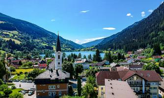 A picturesque mountain landscape with a small lake and colorful houses. In the foreground stands a church with a tall tower.