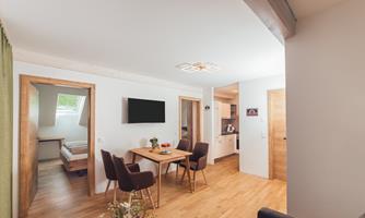A modern apartment with an open living area and wooden flooring. The room is bright and welcoming with a table and chairs as well as a kitchen in the background.
