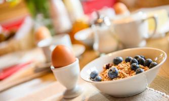 A covered breakfast table with a bowl of muesli and fresh blueberries. Next to the bowl is a soft-boiled egg in an egg cup.