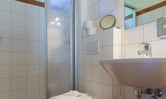A modern bathroom with a shower and a sink. The walls are tiled white and the light is bright.