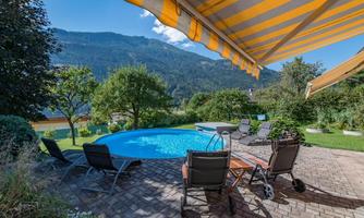 A beautiful garden with a swimming pool and loungers. In the background, there are mountains and a clear blue sky.