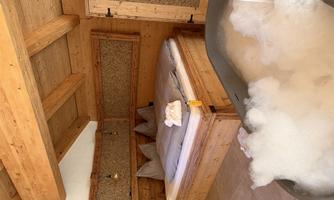 A cozy bedroom with a wooden bed and a modern bathtub full of foam. The warm wood tones create a relaxing atmosphere.