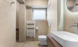 A modern bathroom with a white sink and a toilet. The walls are painted in neutral tones and there is a small window for daylight.