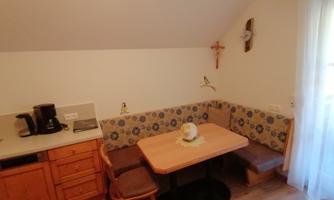 A cozy kitchen area with a wooden log table and a comfortable seating corner. In the background, there is a coffee machine and some decorative elements.