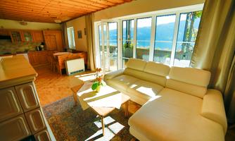 A bright living room with a beige sofa and large windows. The room offers a beautiful view of nature.