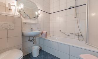A modern bathroom with a bathtub and a shower. The walls are tiled and there is a sink with a mirror.