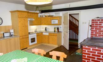 A cozy wooden kitchen design with a green checkered tablecloth. In the background, an open window and a staircase are visible.