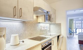 A modern kitchen with light cabinets and stainless steel appliances. It features a cooktop, an oven, and a microwave.