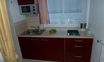 A small, modern kitchen with red cabinets and a window. On the countertop, there is a bowl of grapes.