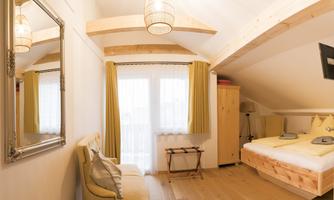 A cozy room with wooden beams and large windows. There is a bed, an armchair, and a mirror on the wall.