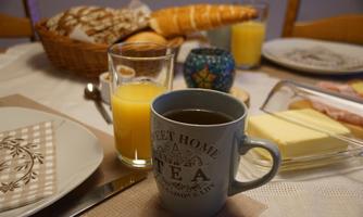 A set breakfast table with a selection of rolls, cheese, and cold cuts. A cup of coffee and a glass of orange juice complete the picture.