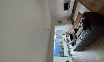 A modern living room with a comfortable sofa and a wooden table. Large windows offer a view of the mountains and plenty of natural light.