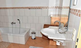 A modern bathroom with a bathtub and a sink. The walls are tiled and the floor is equipped with terracotta tiles.