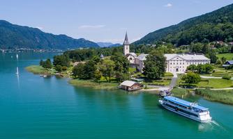A picturesque lake with a boat and an idyllic landscape. In the background, mountains and a church are visible.