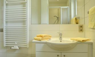 A modern bathroom with white tiles and a bright sink. Towels in yellow are neatly laid out on the table.