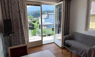 A cozy room with a sofa and a table. Large windows open up a view of the green landscape outside.