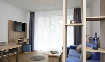 A modern living room with wooden furniture and a blue sofa. Large windows let in plenty of light and provide a cozy space.