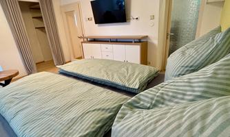 A modern bedroom with two single beds and striped bedspreads. A television hangs on the wall, and there is wardrobe space in the background.