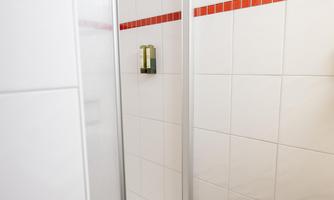 A modern shower with a glass wall and white tiles. The room has a subtle red accent color.