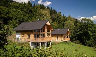 Two modern wooden houses in the midst of a green landscape. In the background, trees and a blue sky can be seen.
