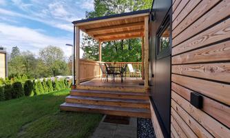 A modern wooden terrace with an outdoor dining area. In the background, green trees and a clear sky can be seen.